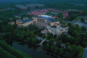 A large, multi-story hotel with a curved facade, surrounded by greenery and a body of water. - Xihai Ecological Garden Vacation Hotel Liu’an (Lu'an)