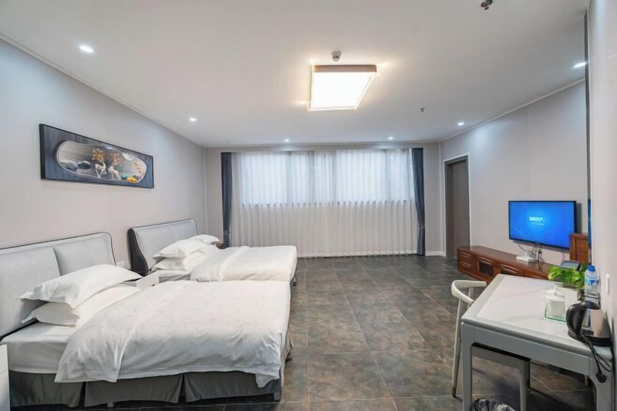 A hotel room with two beds, a desk, a television, and a window with curtains.