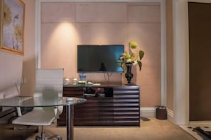 A modern living room with a flat-screen TV mounted on a wall, a glass coffee table, a dark wooden cabinet, and a vase with flowers. - Xihai Ecological Garden Vacation Hotel Liu’an (Lu'an)