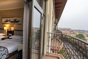 A hotel room with a bed, bedside lamps, a painting, and a balcony with a view of the city. - Xihai Ecological Garden Vacation Hotel Liu’an (Lu'an)