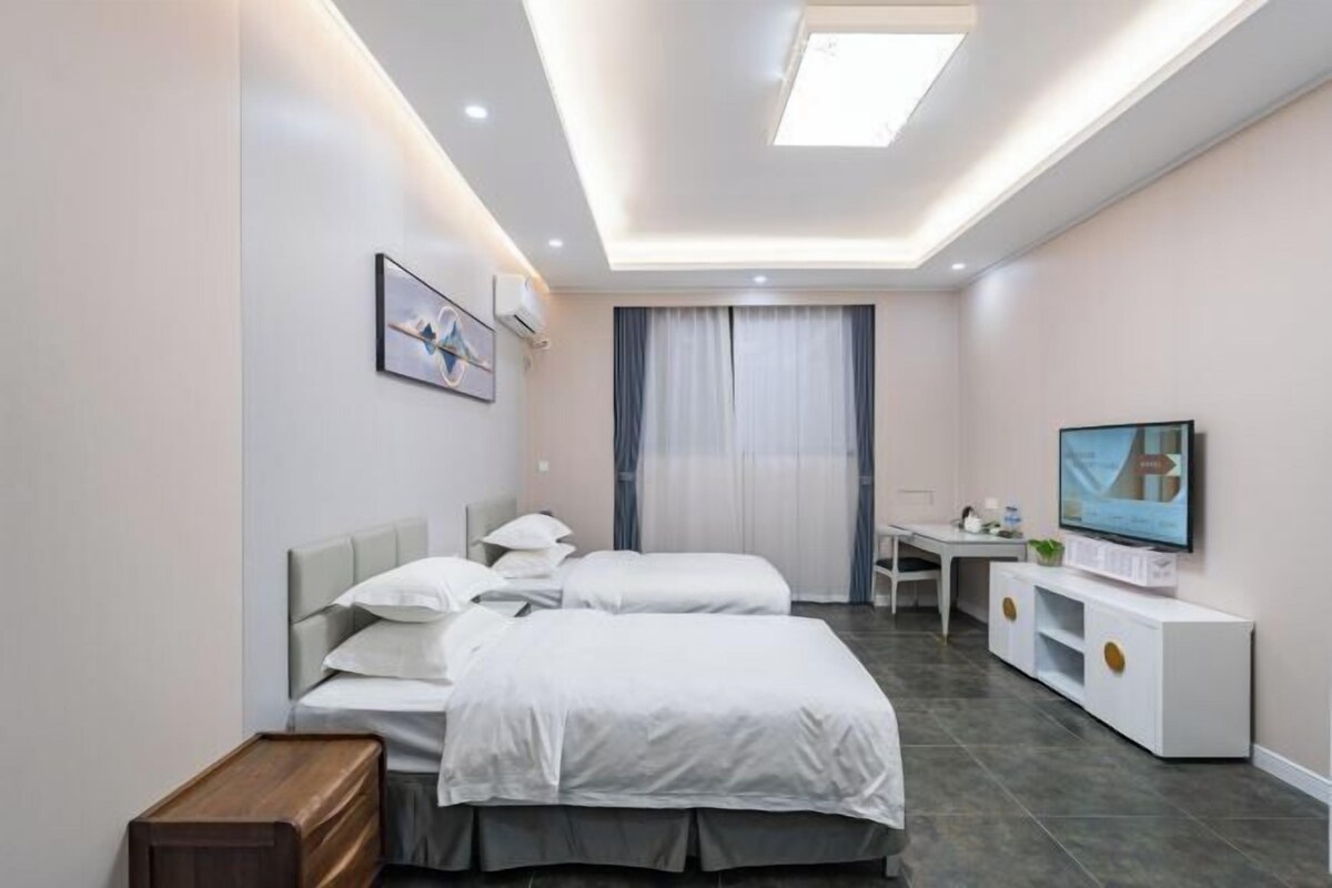 A modern hotel room with a bed, bedside table, TV, and a desk with a chair.