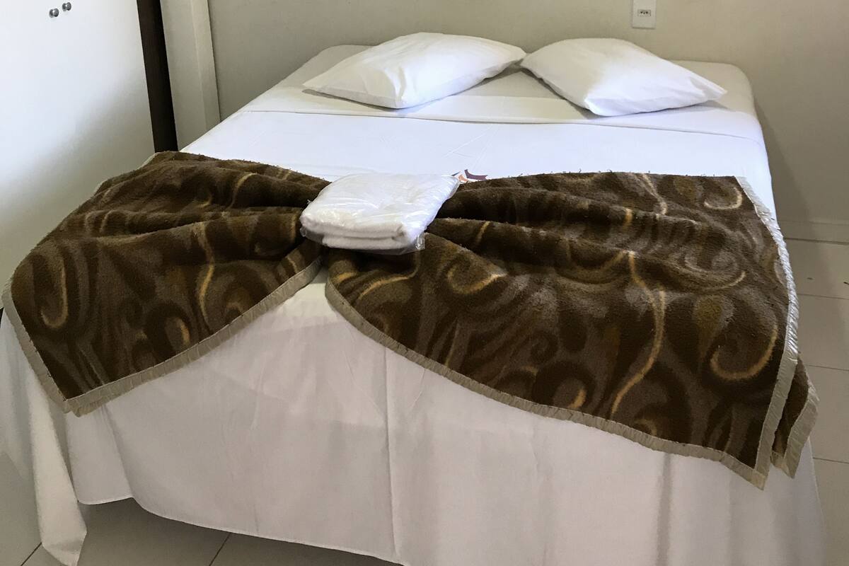A neatly made bed with a brown patterned blanket and white pillows, a framed picture on the wall, and a white door with a small window.