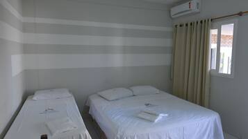 A hotel room with two single beds, a window with curtains, and an air conditioning unit on the wall.