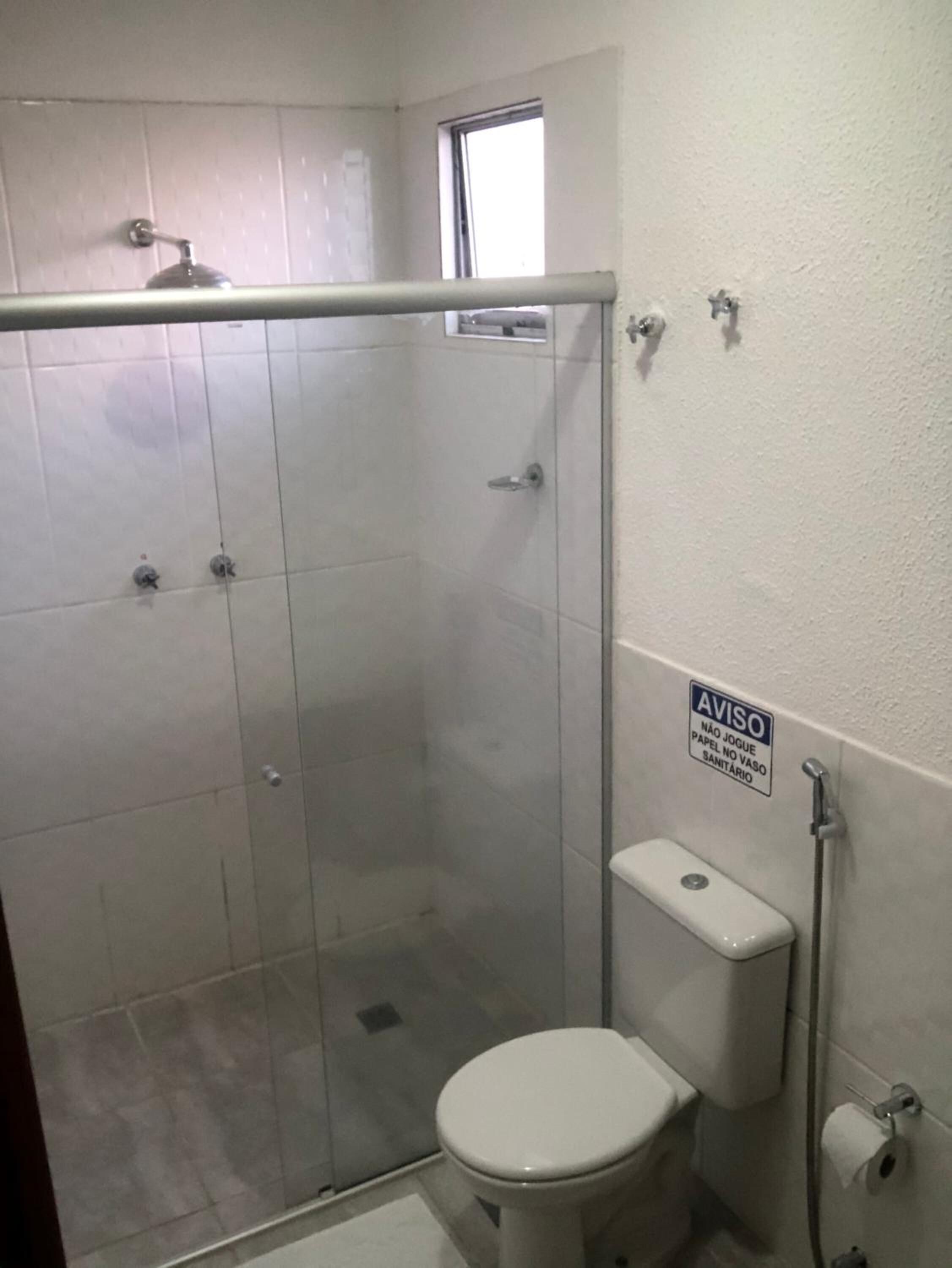 Een badkamer met een douchecabine van glas, een toilet en een bordje aan de muur.