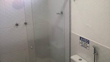 Een badkamer met een douchecabine van glas, een toilet en een bordje aan de muur.