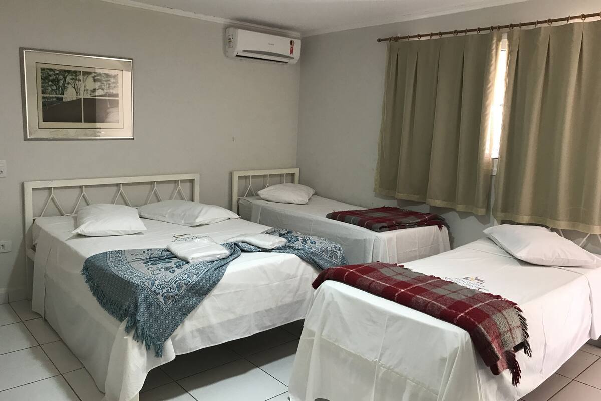 A room with two beds, a framed picture on the wall, and an air conditioning unit.