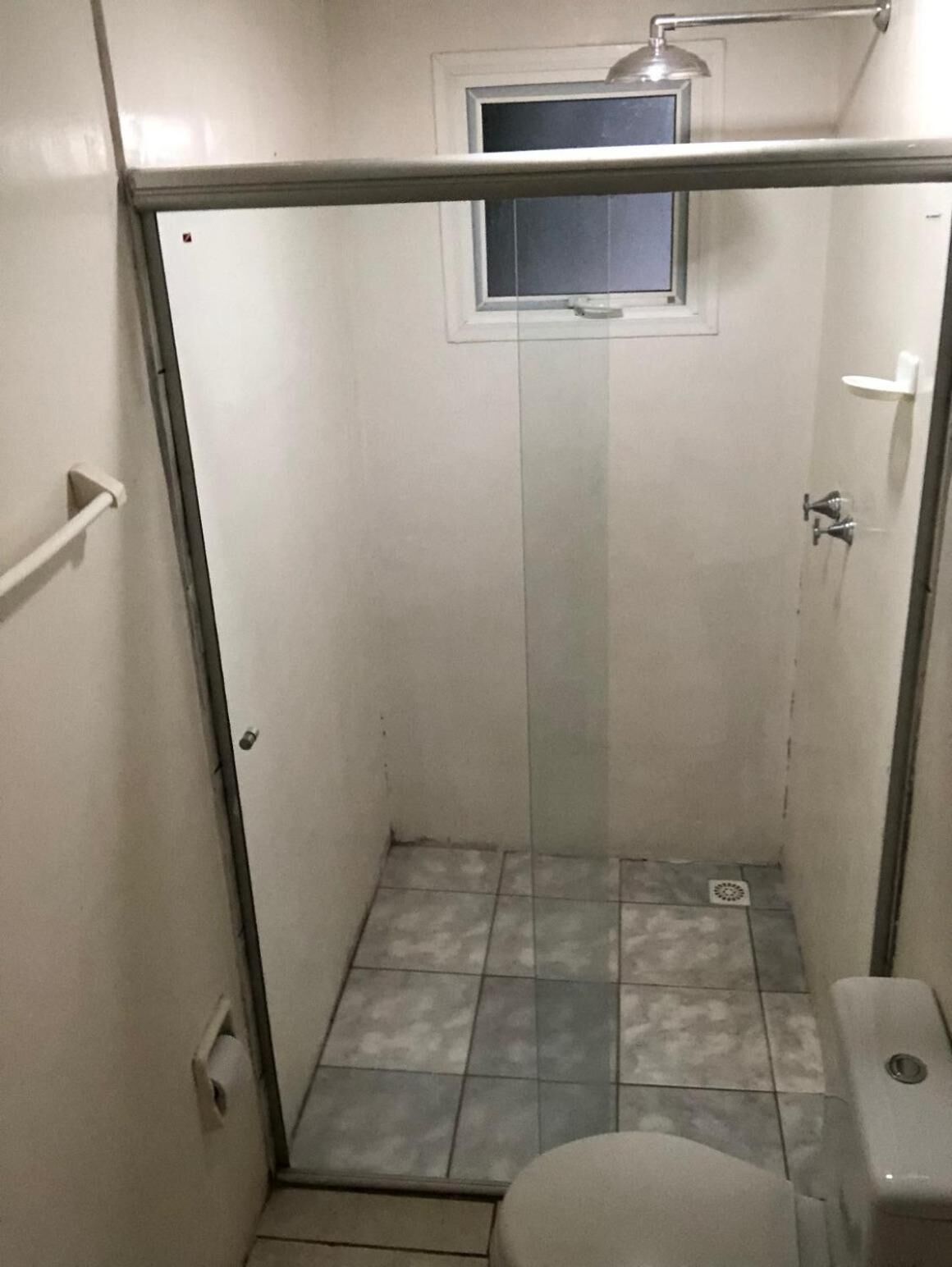 A small, enclosed shower area with a toilet, a window, and a metal door.