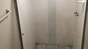A small, enclosed shower area with a toilet, a window, and a metal door.