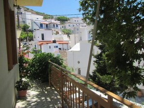 A balcony with a wooden railing overlooking a white building with red-tiled roofs. - Harmony Apartments (Fournoi)