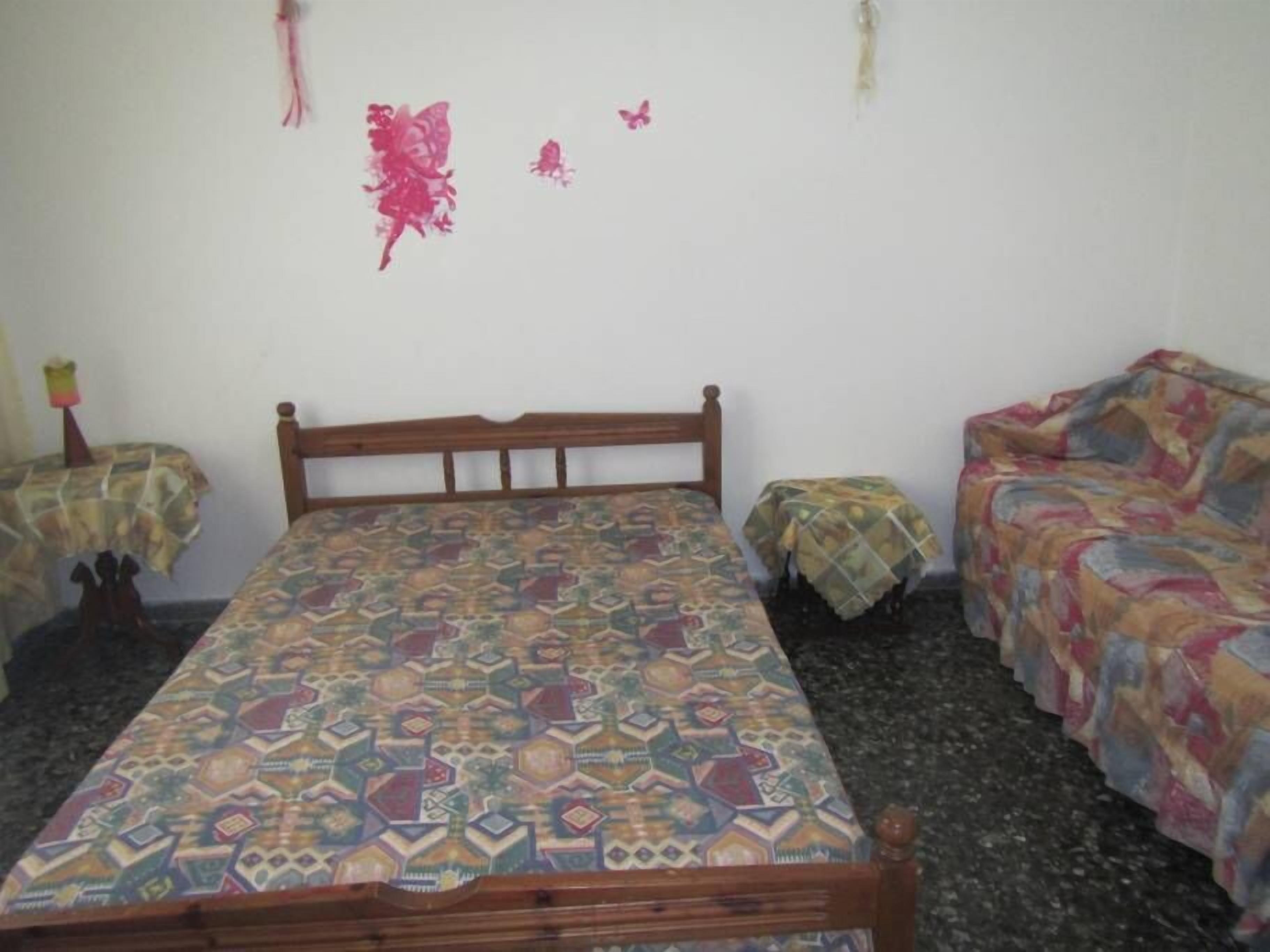 A small, simple room with a bed, a sofa, and two small tables.