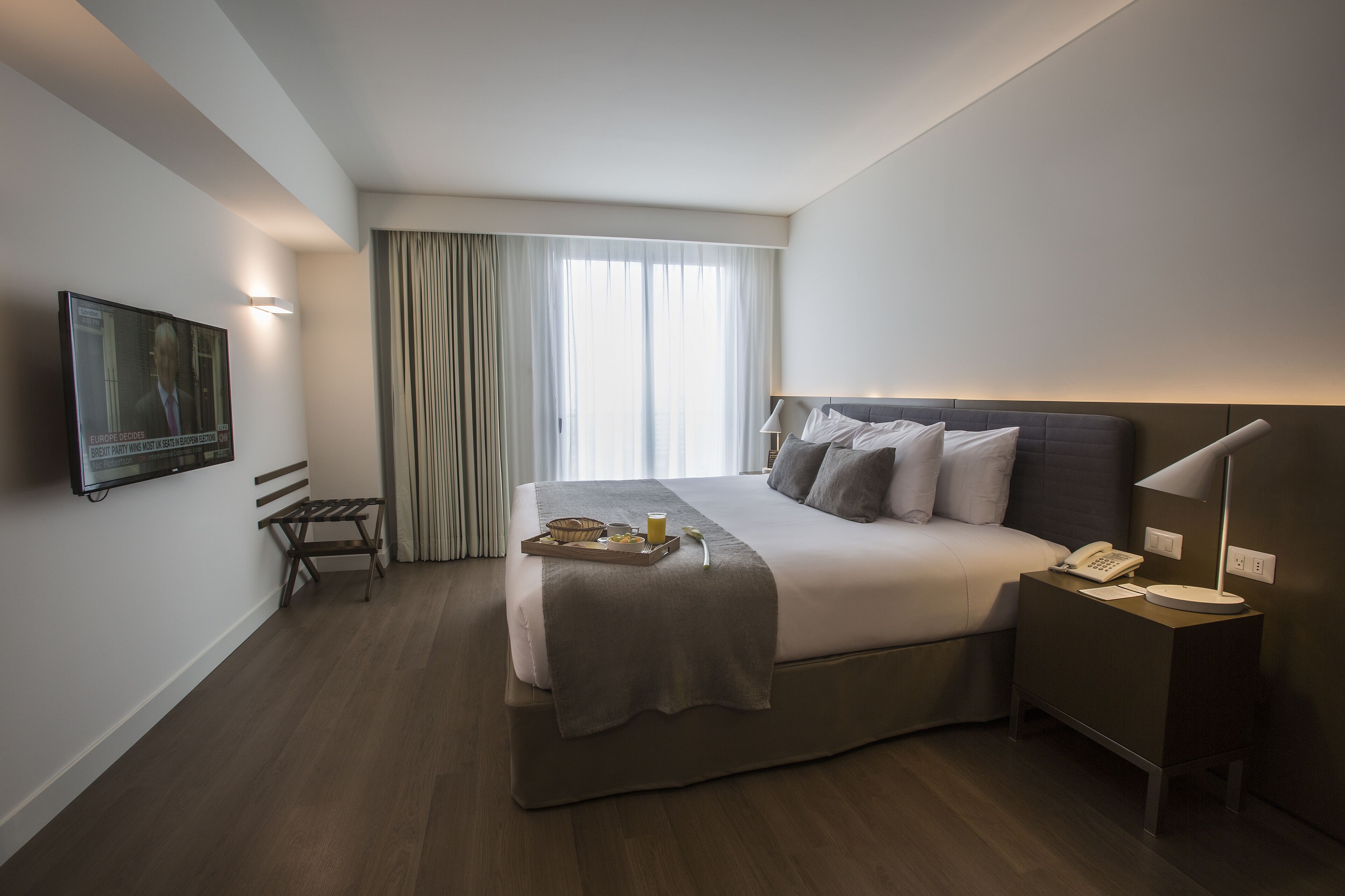 A modern hotel room with a large bed, bedside table, and a TV mounted on the wall.
