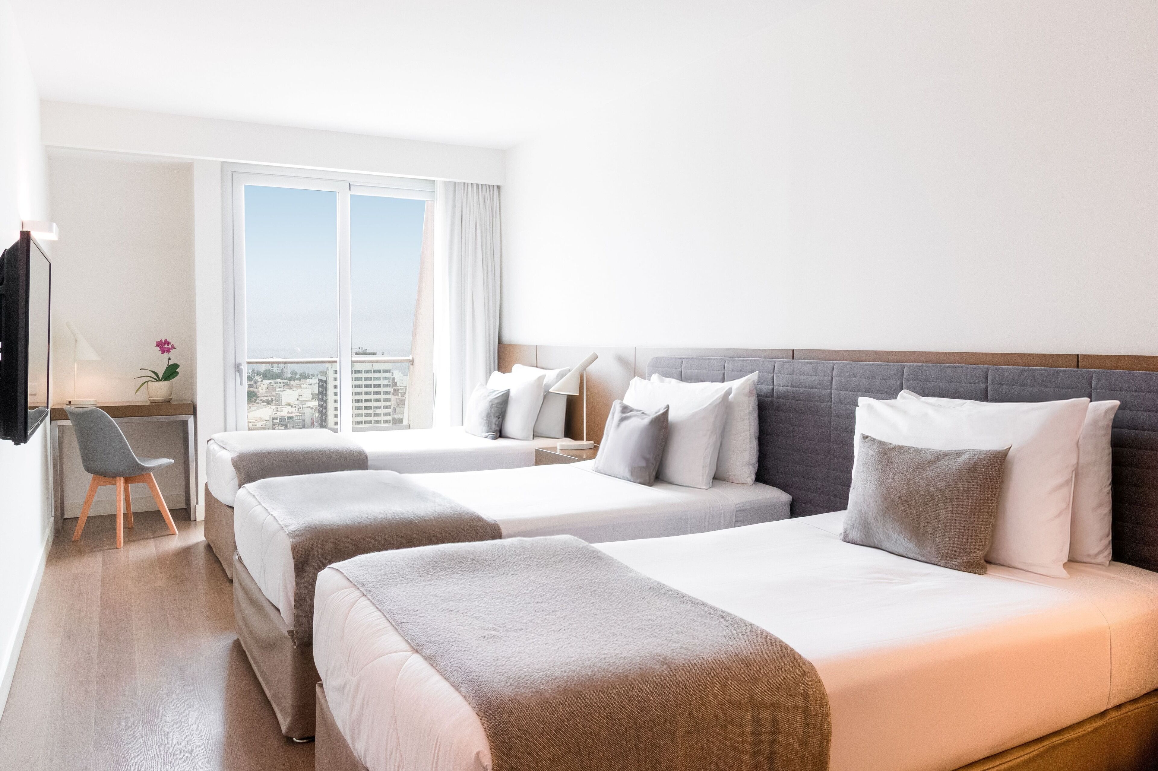 Hotelkamer met twee bedden, een bureau, een stoel en een groot raam met uitzicht op de stad.