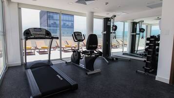 Un gimnasio con cintas de correr, bicicletas estáticas y máquinas de pesas, con ventanas amplias que ofrecen vistas de la ciudad.
