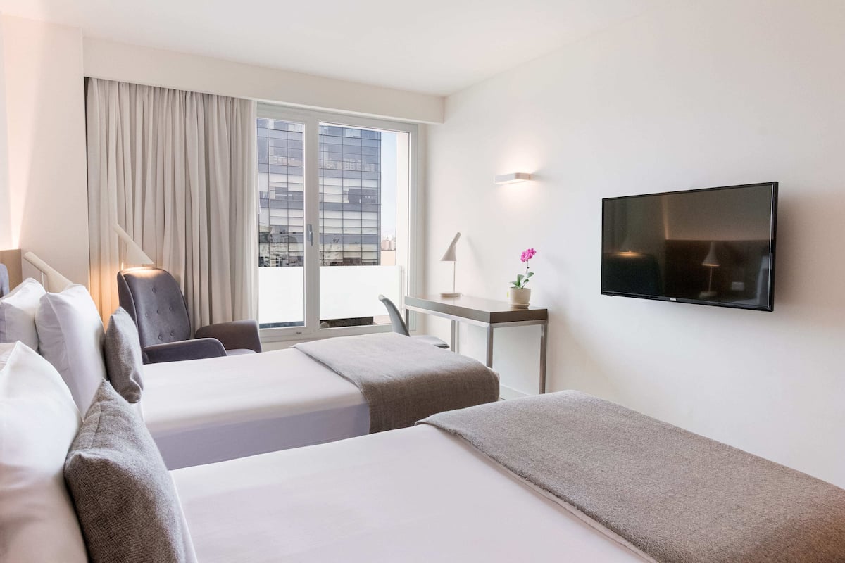 Ein Hotelzimmer mit zwei Betten, einem Schreibtisch, einem Stuhl, einem Fernseher und einem Fenster mit Vorhängen.