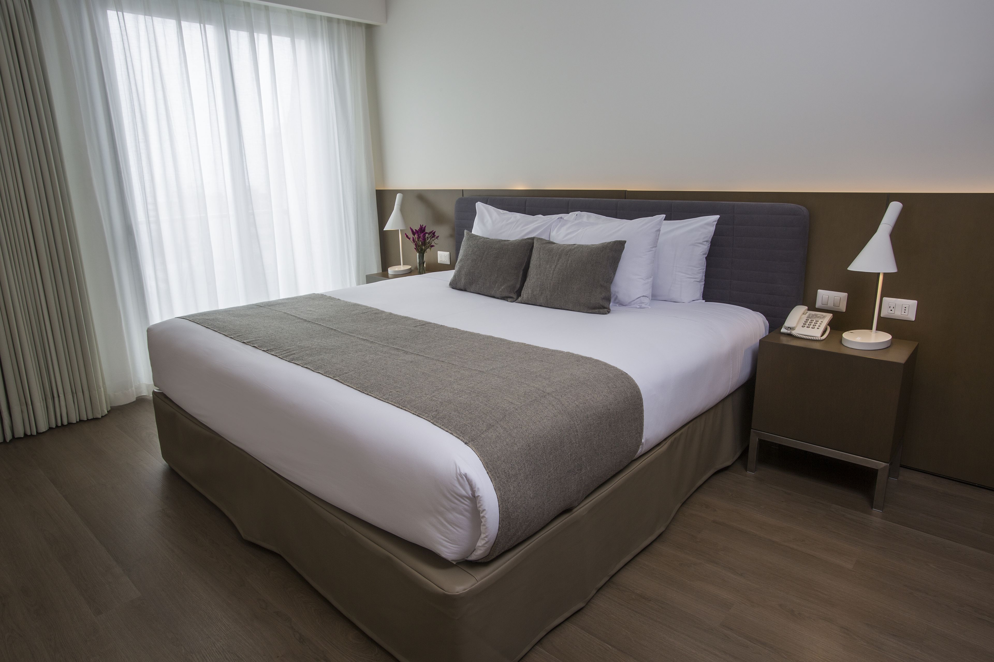 A hotel room with a large bed, a bedside table with a lamp, and a phone.