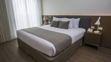 A hotel room with a large bed, a bedside table with a lamp, and a phone.