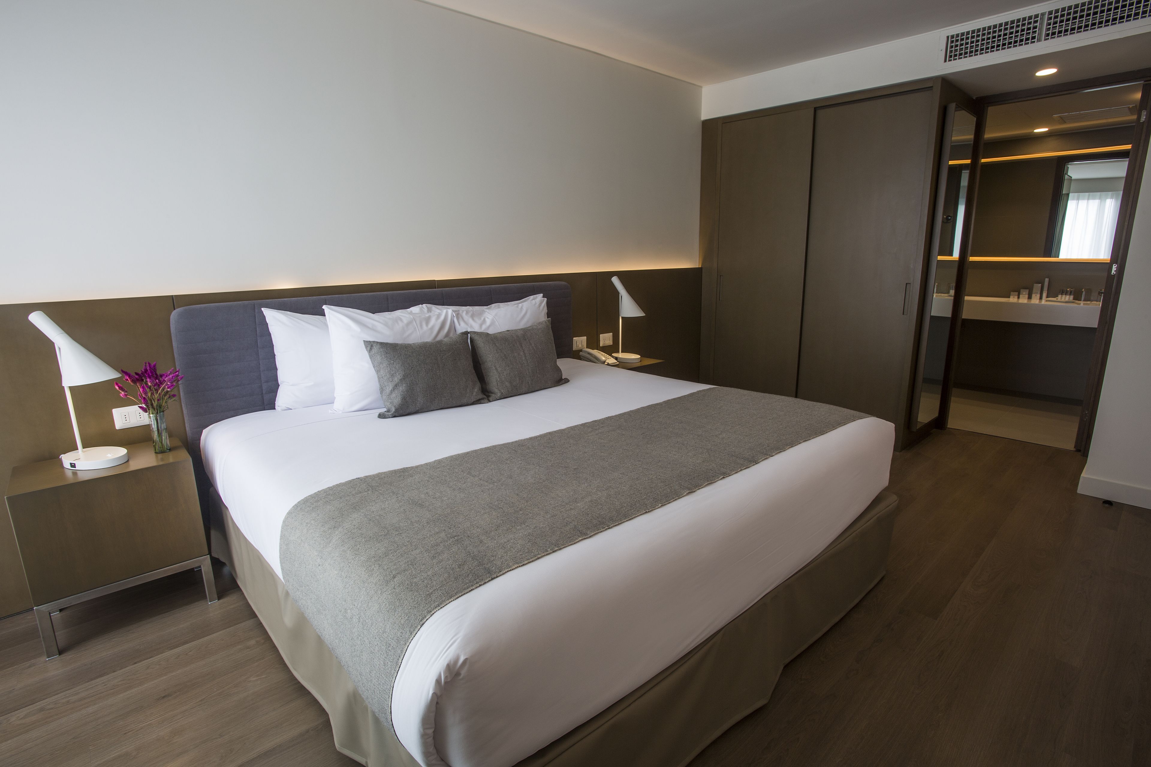 Una habitación de hotel moderna con una cama grande, mesitas de noche, un armario y un espejo.