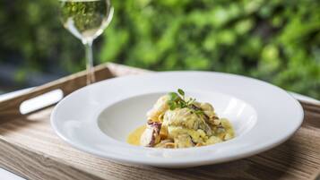 Un plato blanco con un guiso cremoso, una copa de vino blanco y una mesa de madera sobre un fondo verde desenfocado.