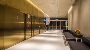 Un hall d’entrée moderne avec un long couloir, des ascenseurs, un espace d’accueil et un coin salon agrémenté d’un vase de fleurs.