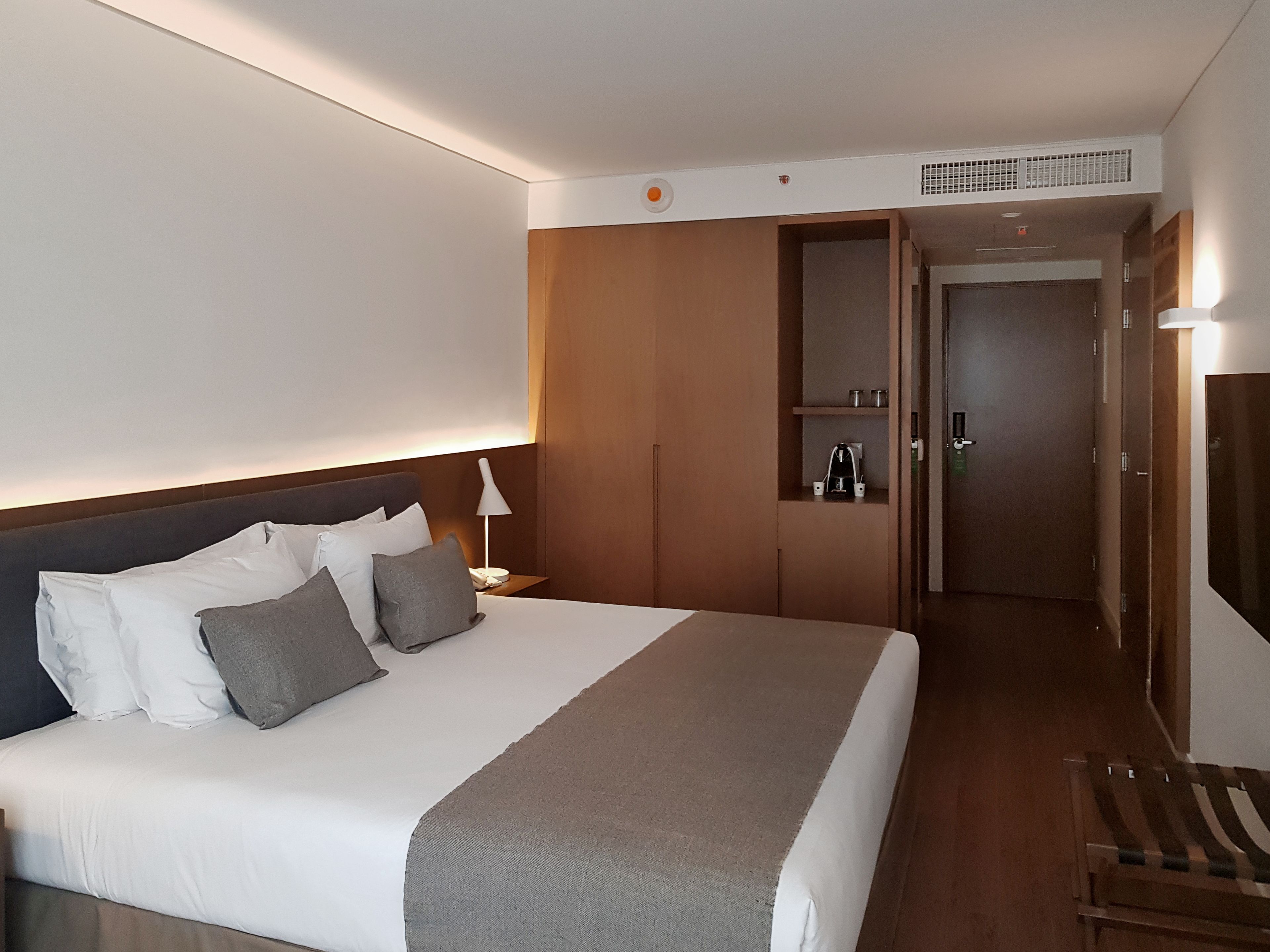 Une chambre d’hôtel avec un grand lit, une table de chevet avec une lampe, une armoire et un miroir au mur.