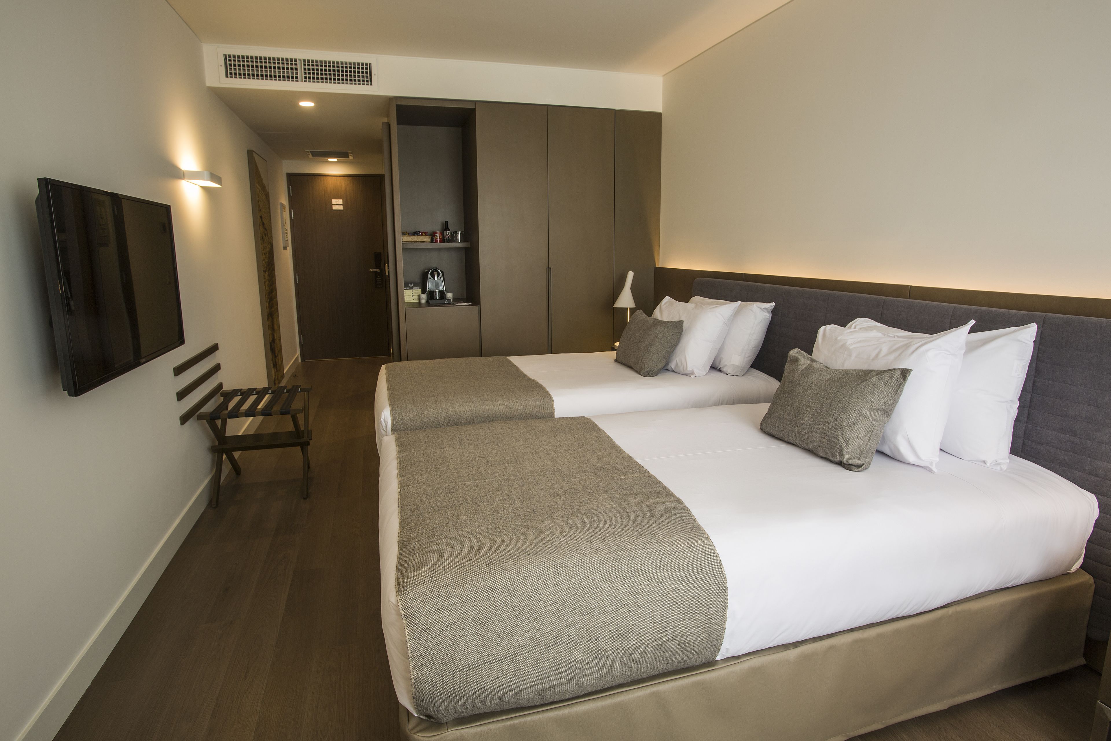 A hotel room with two beds, a bench, a TV, and a wardrobe.