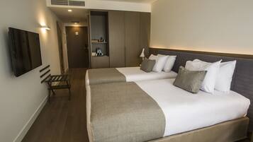 A hotel room with two beds, a bench, a TV, and a wardrobe.