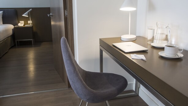A hotel room with a bed, a desk with a laptop, a chair, a lamp, a pitcher, and a cup. - Dazzler by Wyndham Lima San Isidro (Lima)