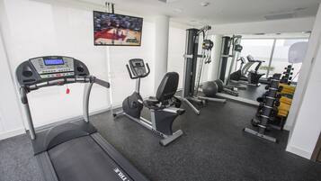 Gimnasio con cintas de correr, máquinas de pesas y una pantalla de televisión mostrando un evento deportivo.