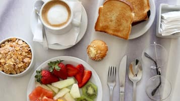 Una mesa con desayuno: tostadas, cereal, fruta, café y jugo.