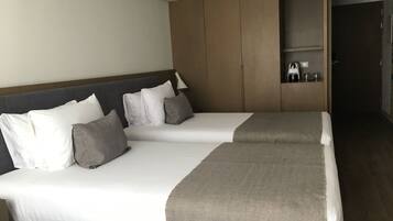 A hotel room with two beds, a wooden headboard, a small shelf with toiletries, and a dark wooden door.
