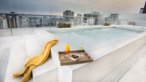 A rooftop pool area with a glass railing, a city view, a wooden tray with a drink and snacks, and a yellow towel. - Dazzler by Wyndham Lima San Isidro (Lima)
