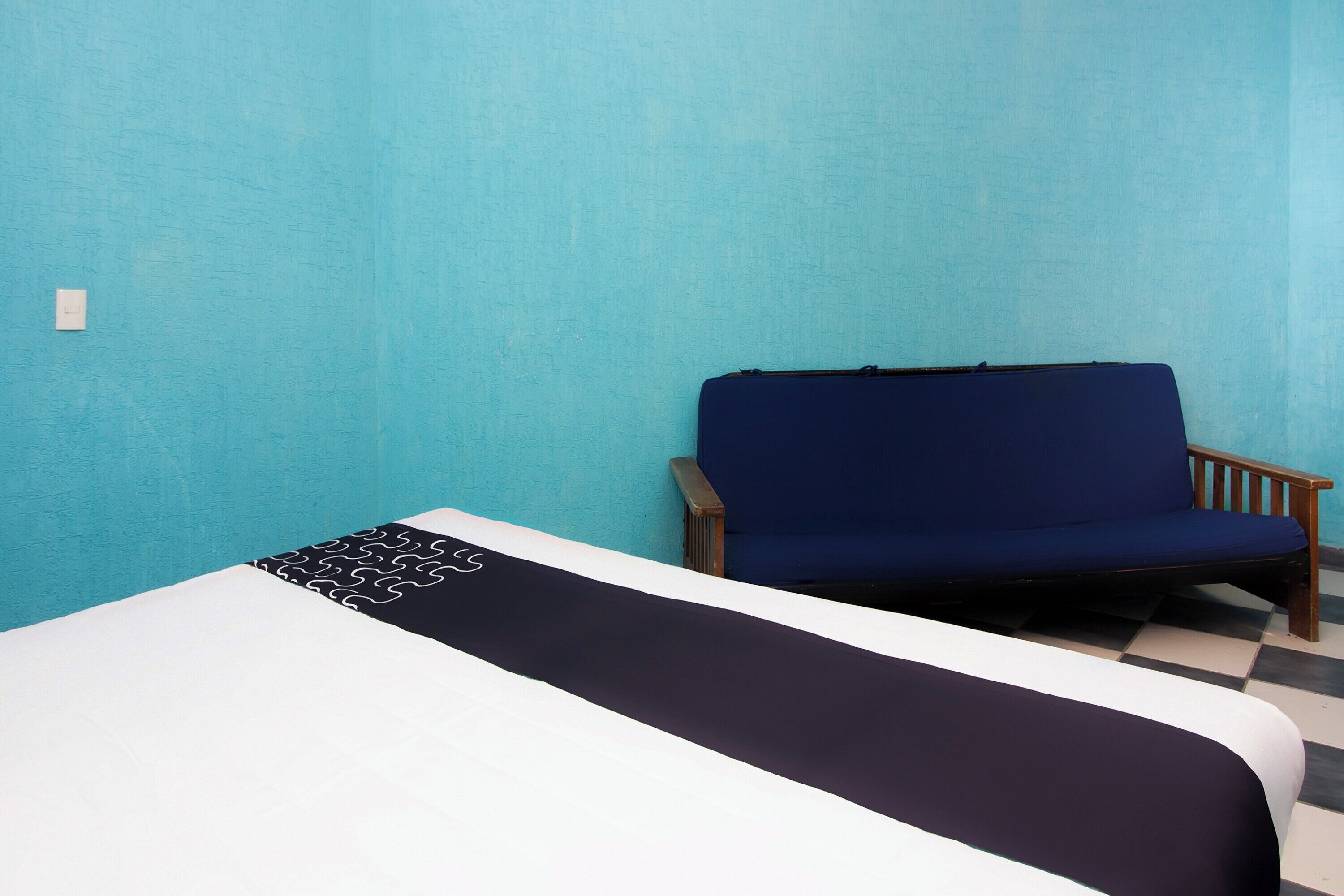 Una habitación con una cama, una silla azul y un suelo a cuadros.