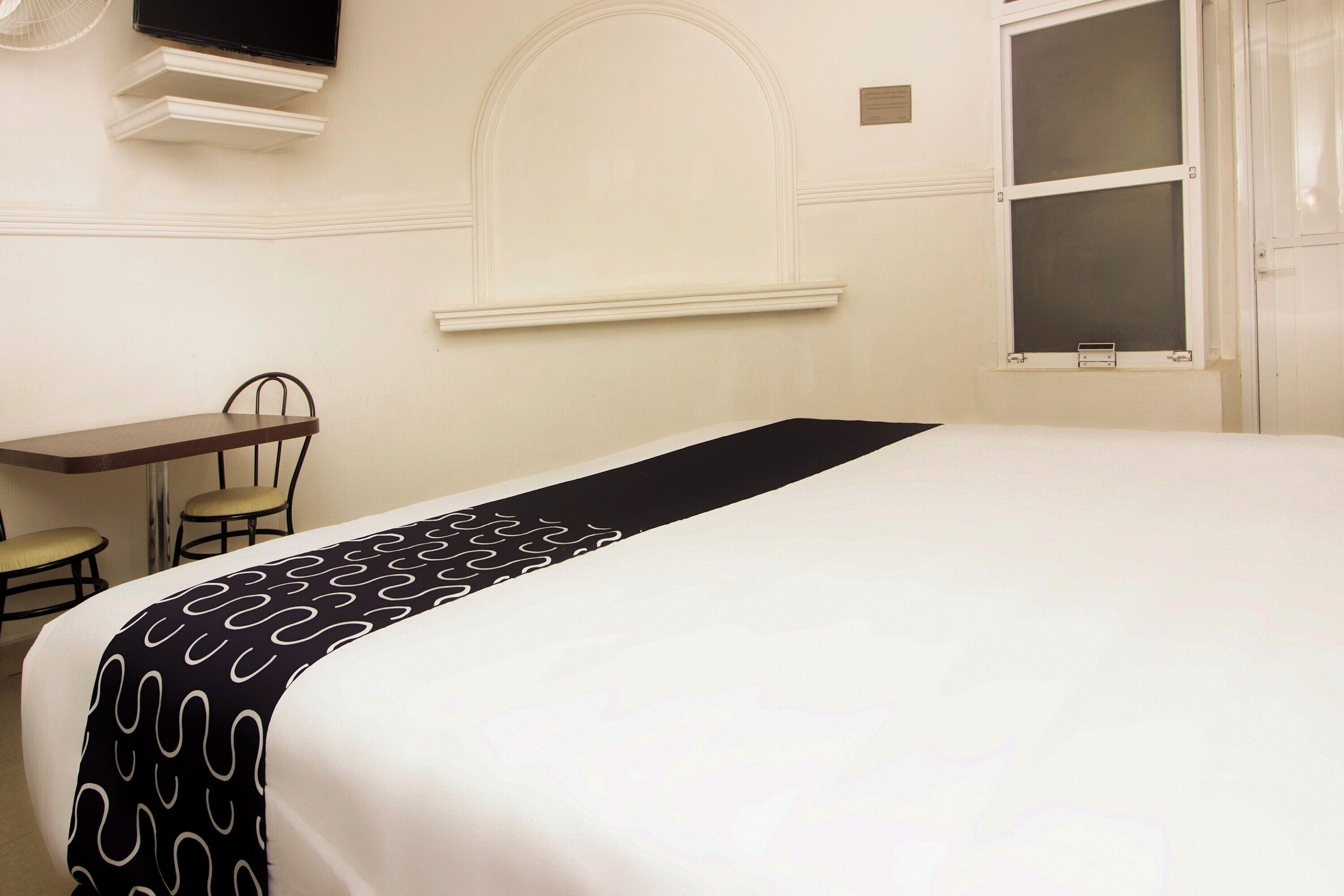Una habitación de hotel con una cama, un escritorio, una silla y un televisor montado en la pared.