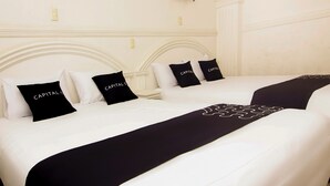 Habitación de hotel con dos camas, cada una con ropa de cama blanca y detalles en negro, incluyendo almohadas y una manta.