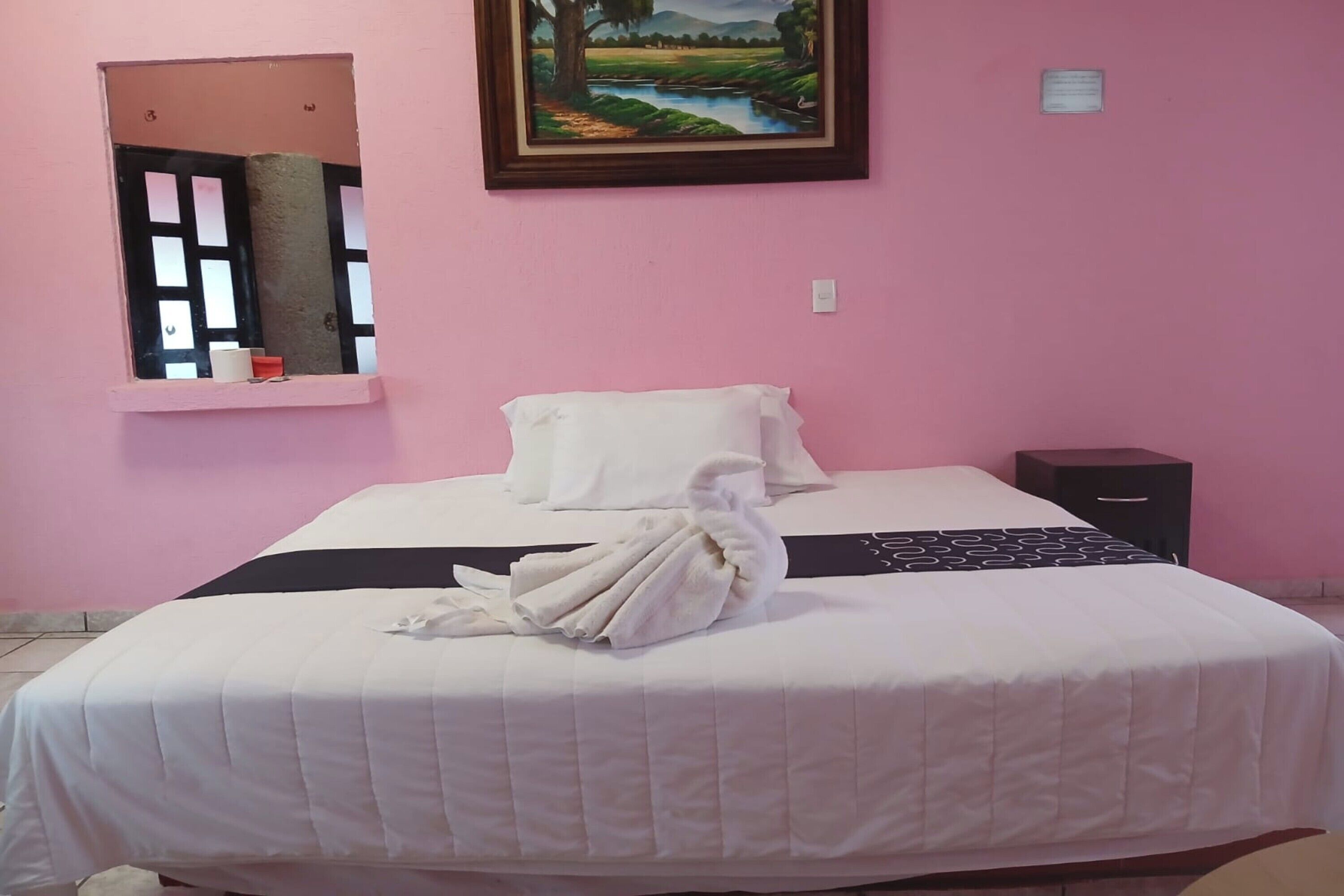 Una habitación de hotel con cama, ventana con vistas, un cuadro en la pared y una mesita de noche.