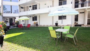 Un patio con mobiliario exterior, piscina y un edificio con varios balcones.
