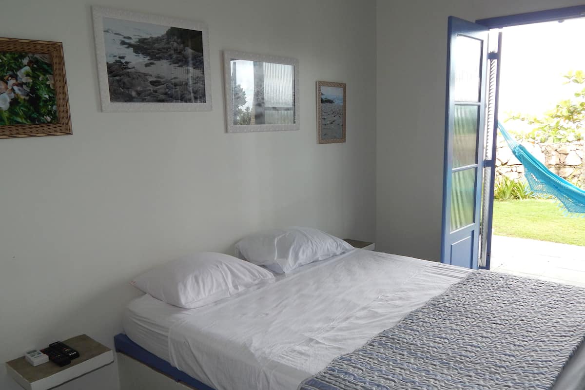 A bedroom with a bed, a nightstand, and a window with a view of a garden.
