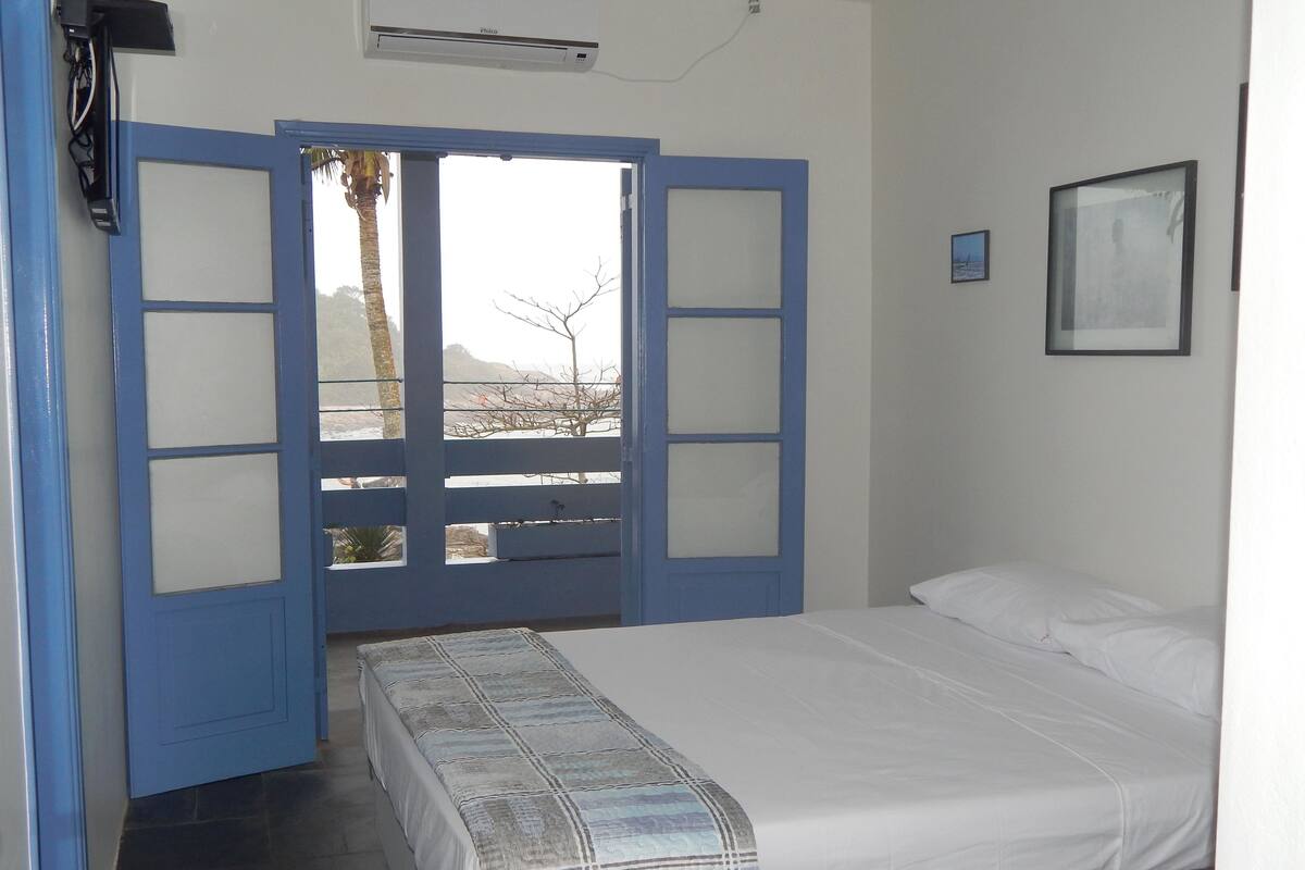 A bedroom with a bed, a window with a view, and a wall-mounted air conditioner.