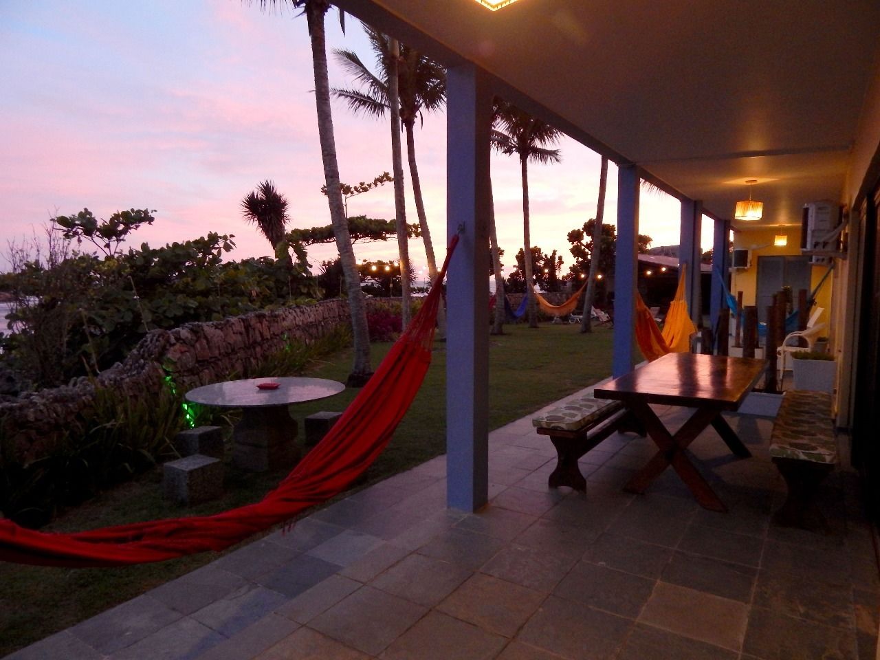 A covered outdoor area with a table and benches, surrounded by palm trees and a stone wall.