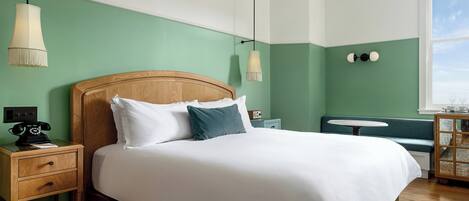A neatly made bed in a room with green walls, a wooden headboard, and a small bedside table with a lamp.