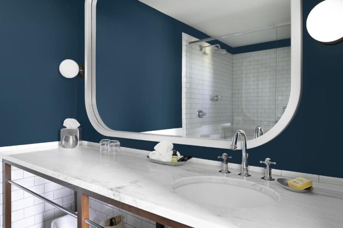 A modern bathroom with a white marble sink, a large mirror, and a shower area visible in the background.