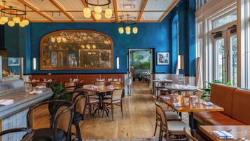 Un interior de restaurante con mesas de madera, sillas de mimbre y una pared azul de acento.