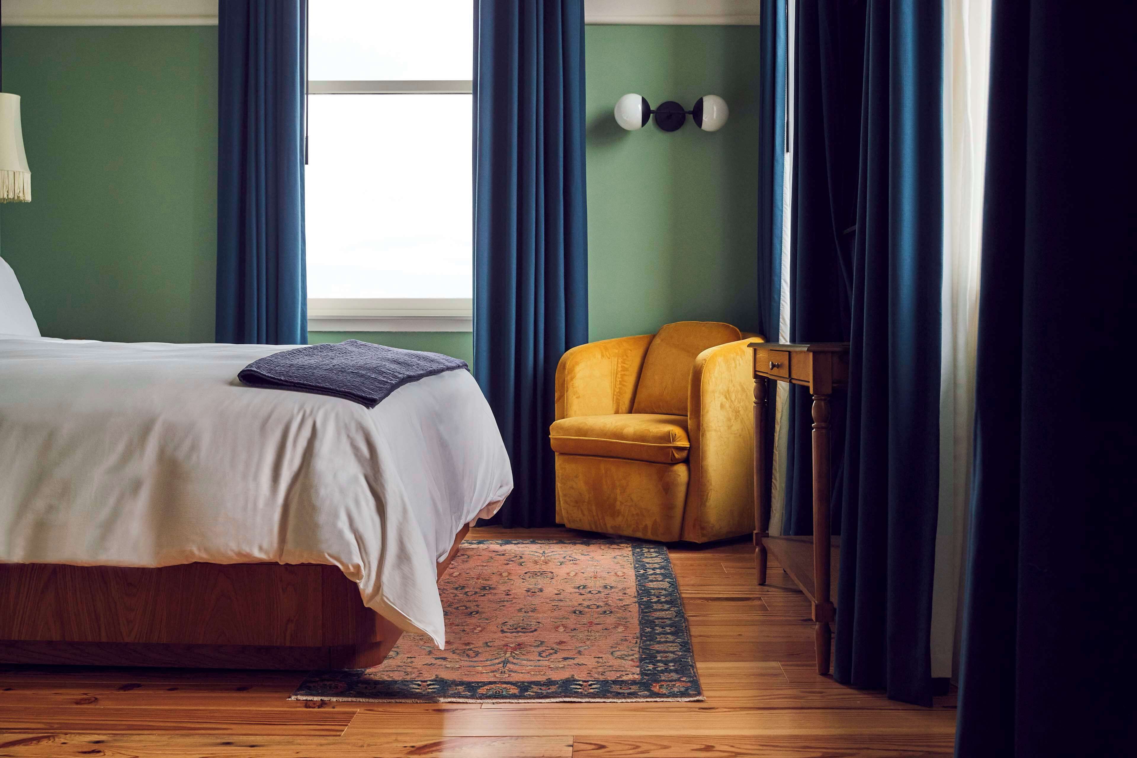 A bedroom with a bed, a chair, a rug, and curtains.