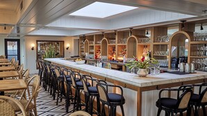 Zona de bar con estantes de madera, taburetes y una barra alargada.
