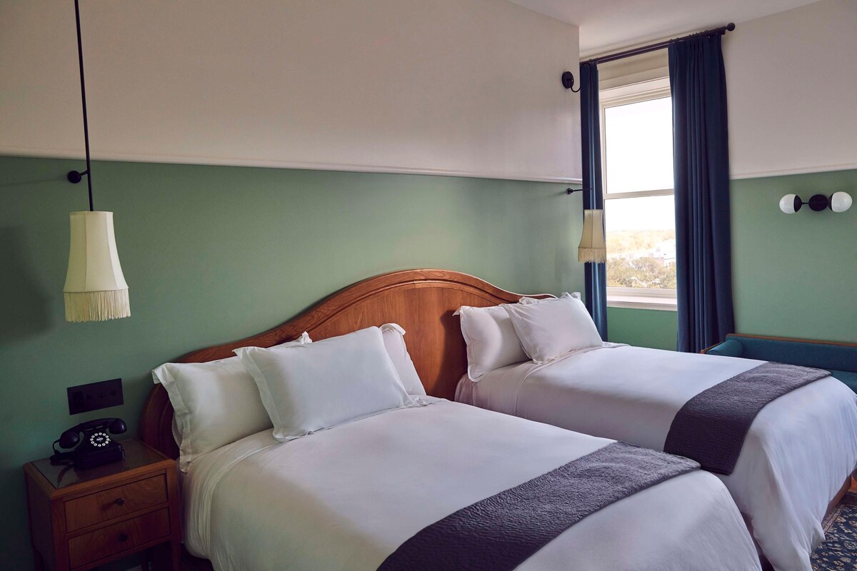 A hotel room with two beds, a nightstand with a telephone, and a window with curtains.