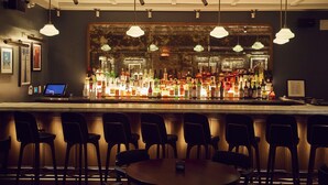 Una zona de bar con una barra larga, varias luces colgantes y varias sillas y mesas.
