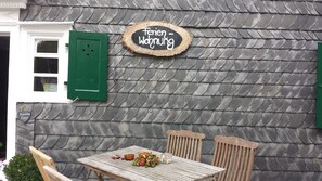 Une façade rustique avec un mur en pierre, une table en bois agrémentée d’un arrangement floral et une enseigne indiquant « Ferienwohnung ».