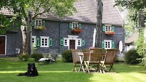 Ein Steinhaus mit gr ünen Fensterläden, einem Rasen und Gartenmöbeln.