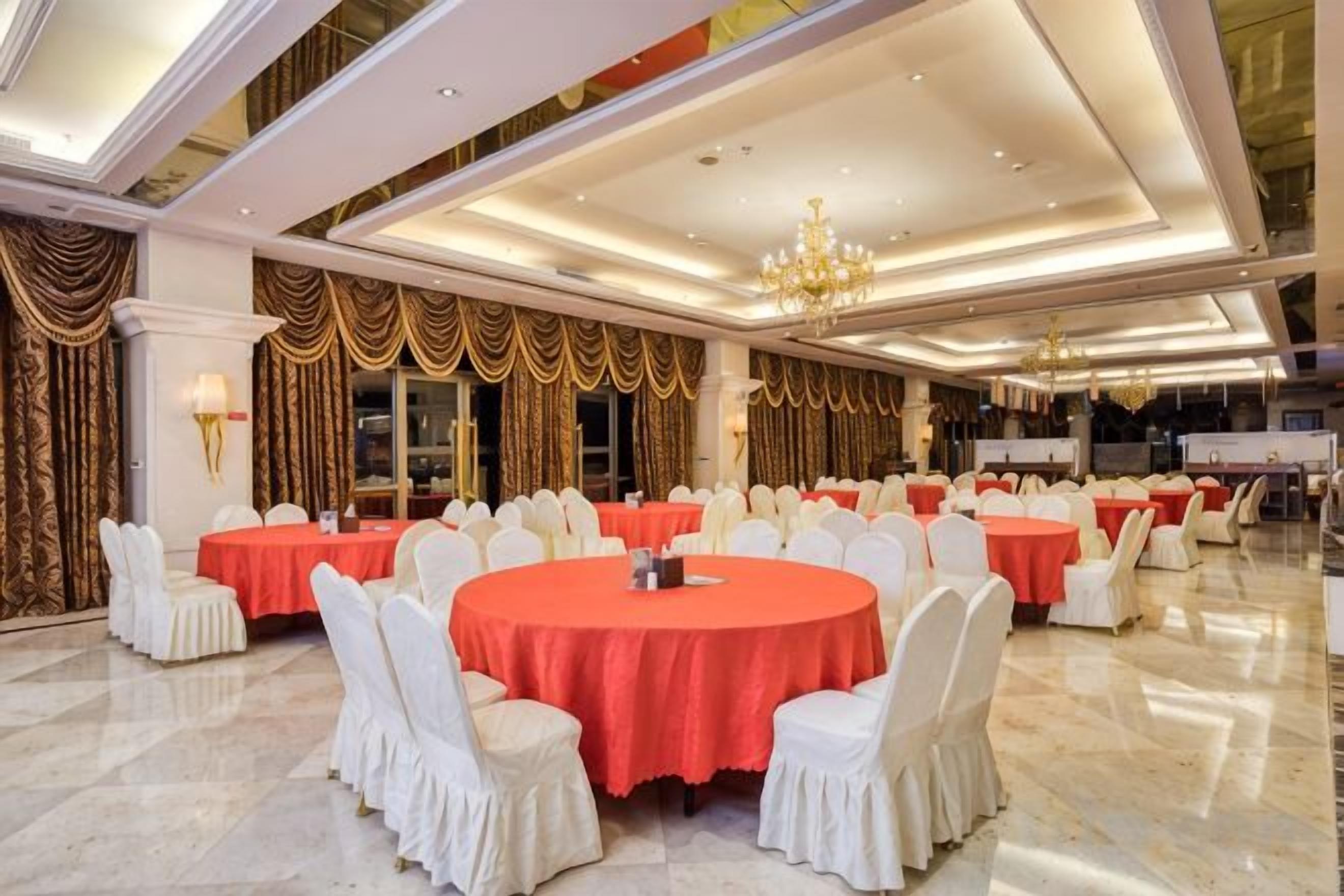 A banquet hall with round tables, white chairs, and red tablecloths.