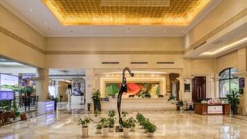 A spacious lobby with a high ceiling, a reception desk, and potted plants.
